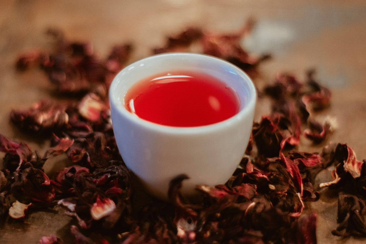 white teacup with red liquid and loose-leaf tea around it