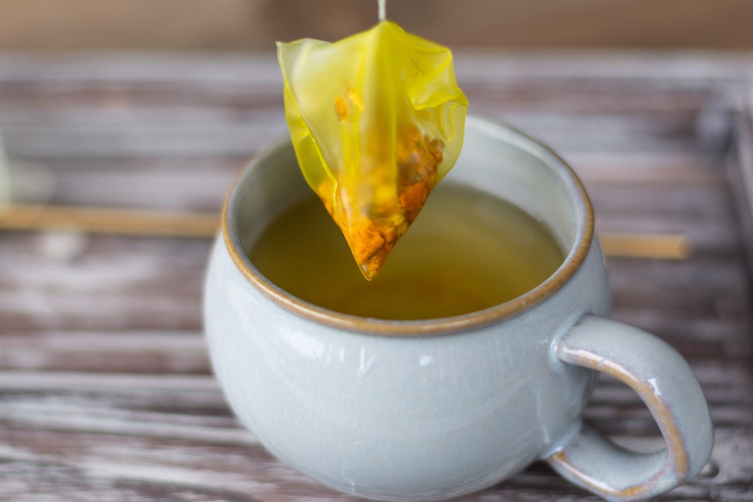 A pyramid shaped turmeric ginger tea bag dunking in a mug